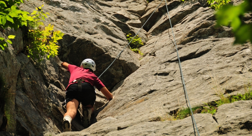 A person wearing safety gear is secured by ropes as they climb a rock wall. 